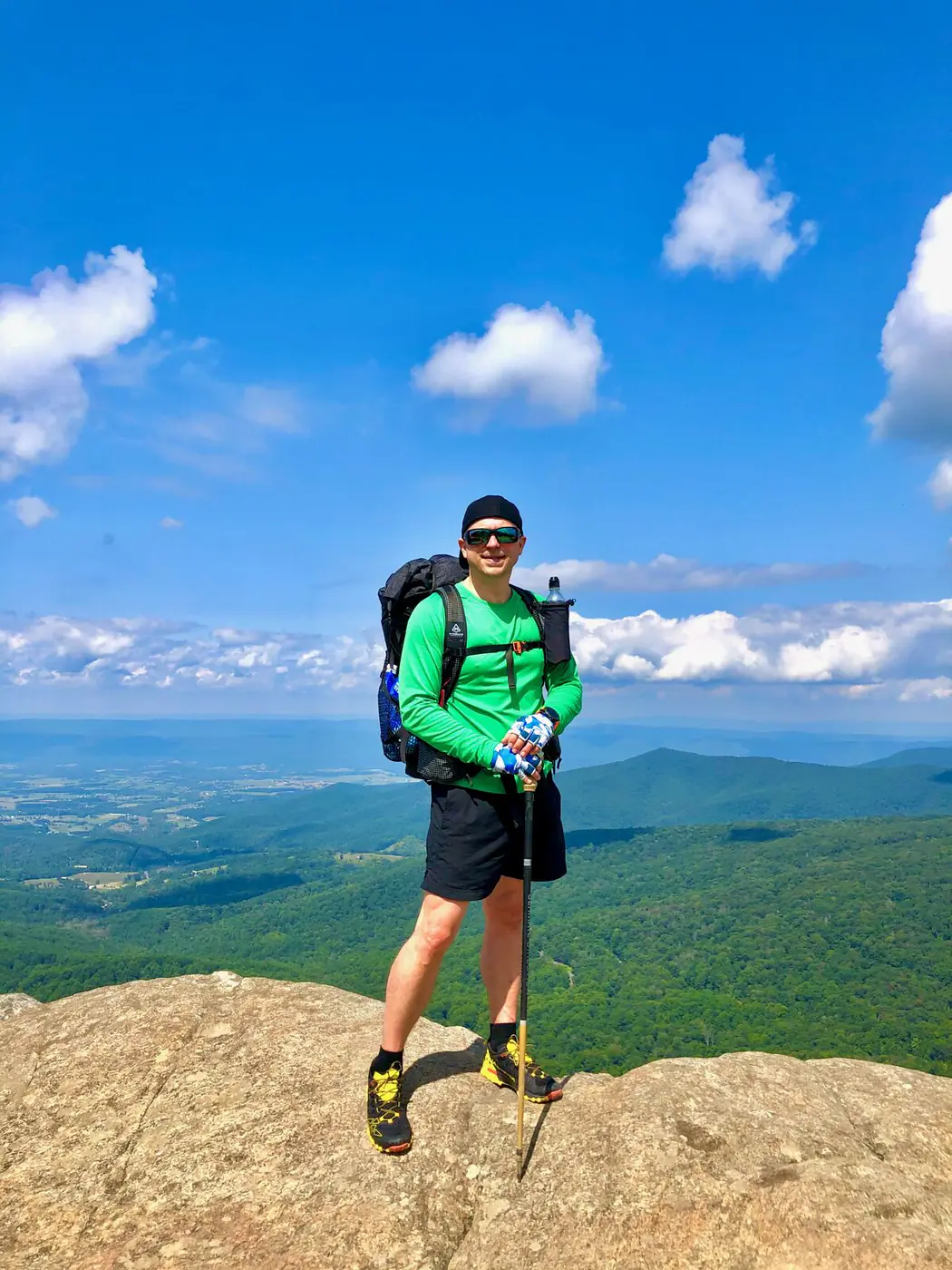 Brian Vinci standing on a mountain summit with trekking poles and a hiking pack